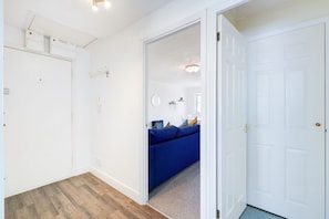 A hallway with a blue sofa, white walls, and a wooden floor.