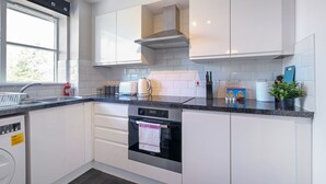 A modern kitchen with white cabinets, a stainless steel oven, and a black granite countertop. - 2 bed luxury apartment (Enfield)
