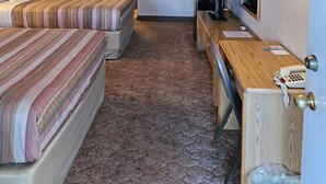 Ein Hotelzimmer mit zwei Betten, einem Schreibtisch, einem Telefon, einem Mülleimer und einem Spiegel.