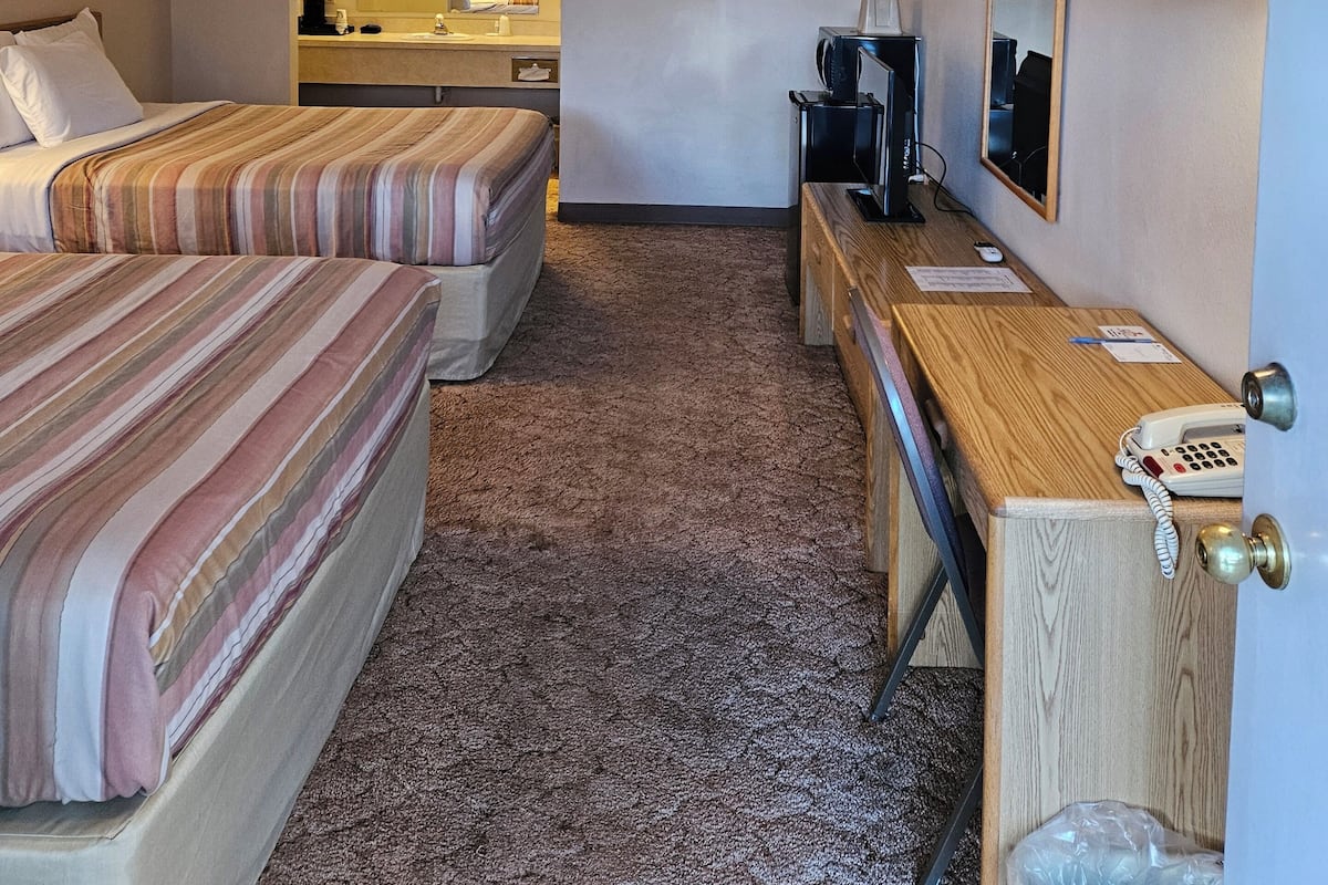 A hotel room with two beds, a desk, a telephone, a trash bin, and a mirror.