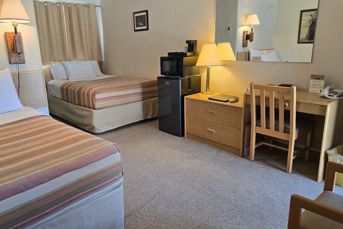 A hotel room with two beds, a desk, a chair, a desk lamp, a telephone, and a microwave.