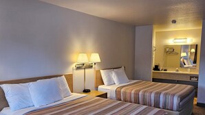 Ein Hotelzimmer mit zwei Betten, einem Nachttisch, einer Lampe, einem Spiegel und einem Teppichboden.