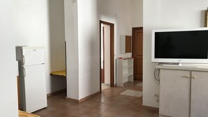 A hallway with a white refrigerator, a television on a cabinet, and a wooden door in the background.