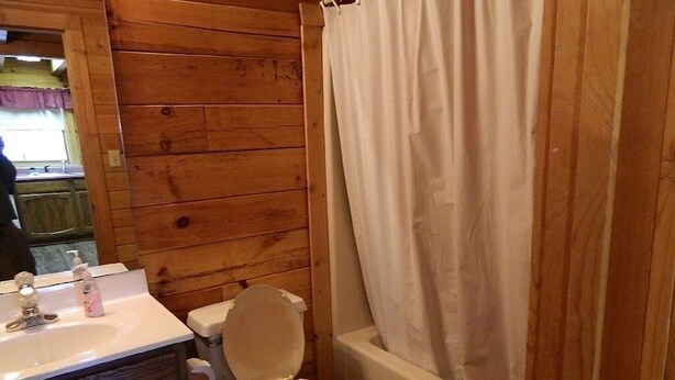 Baño de cabaña de madera con inodoro, lavabo y bañera.