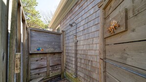 Un espace de douche extérieur en bois, doté d’un tuyau en métal et d’une plaque décorative représentant un poulpe, fixée au mur.