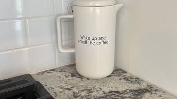 Una cocina con paredes de azulejos blancos, una cafetera blanca con tapa y una encimera de granito.
