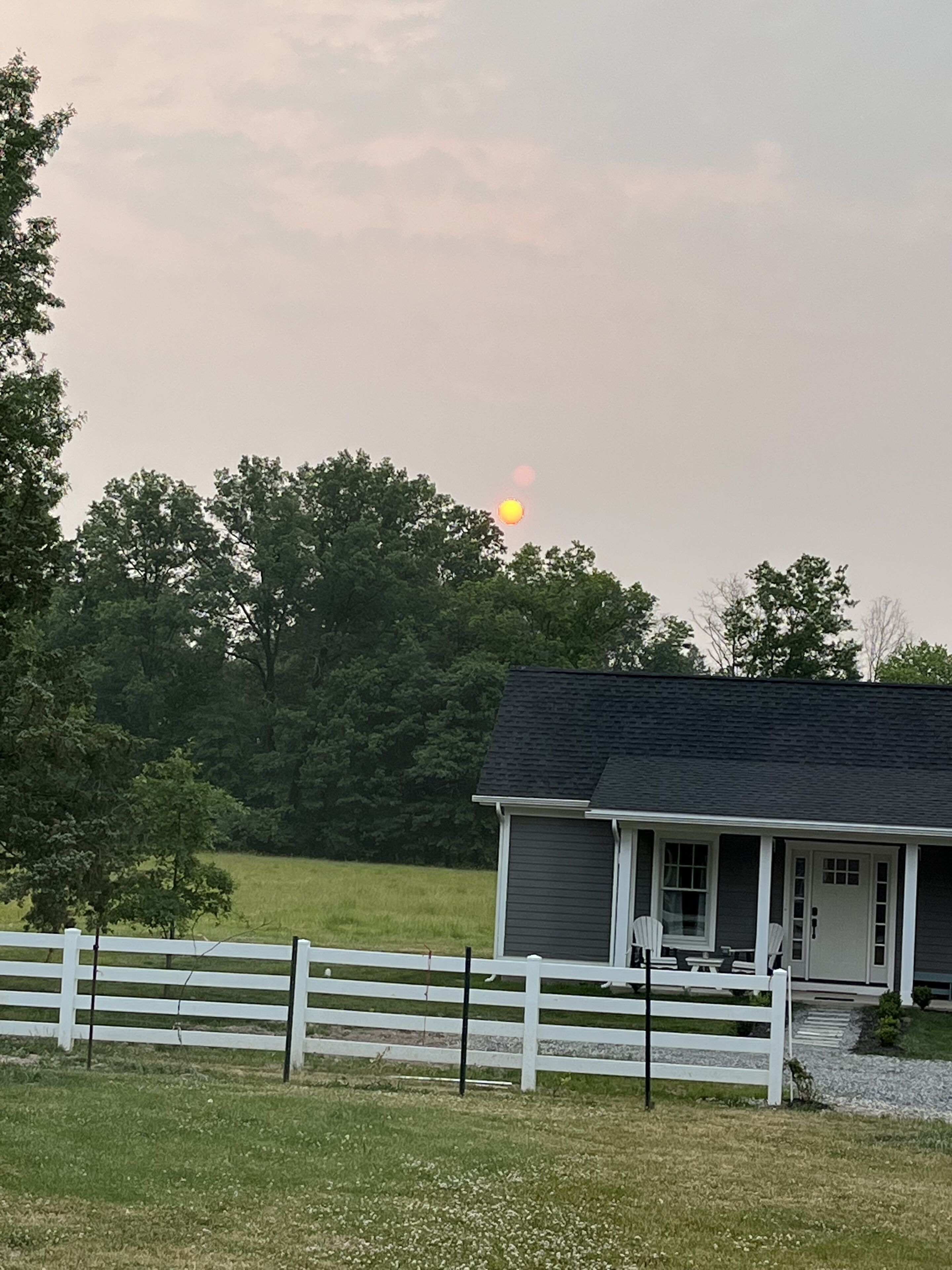 A house with a porch, a fenced yard, and trees in the background.