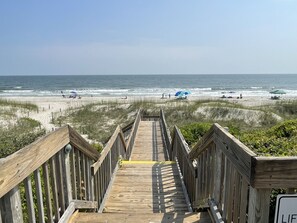 Een houten looppad dat naar een strand leidt, met mensen en parasols.