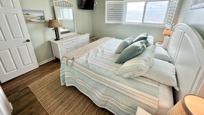 A bedroom with a bed, dresser, TV, and windows. - Sea Turtle Sanctuary-Ocean Front Condo on Perfect Private Beach!  (Oak Island)