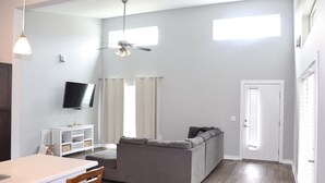 A living room with a gray sofa, a TV mounted on the wall, a ceiling fan, and a white door. - Modern home near downtown Hendersonville (Hendersonville)