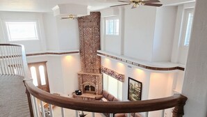 A spacious living area with a fireplace, a high ceiling, and a staircase with a wooden railing.