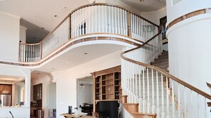 A spacious living area with a curved staircase, a wooden entertainment unit, and a comfortable seating area.