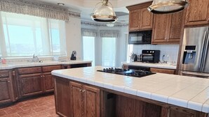 A spacious kitchen with a large island, wooden cabinets, stainless steel appliances, and pendant lighting.