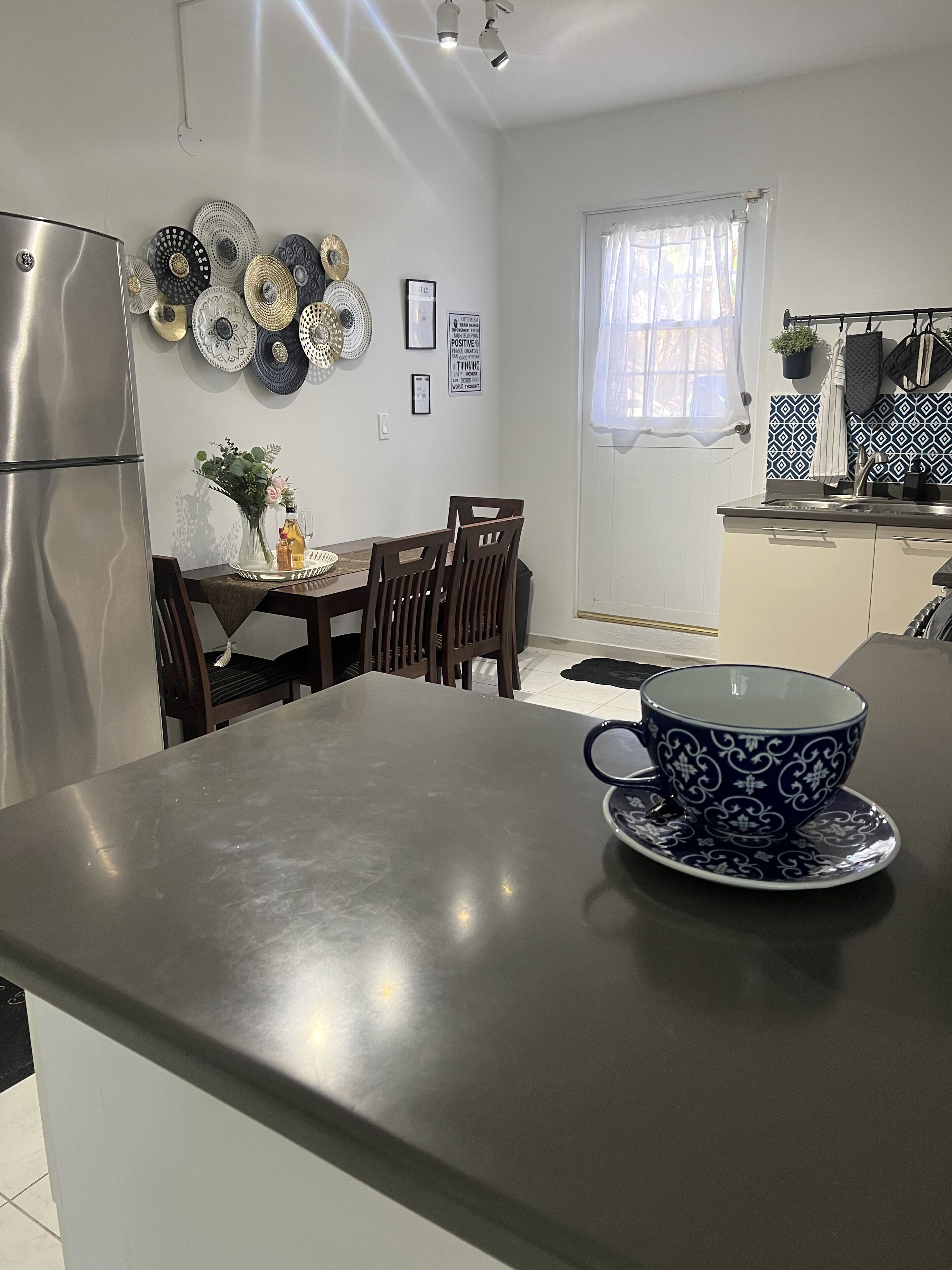 Eine moderne Küche mit einem Edelstahl-Kühlschrank, einem Esstisch mit Stühlen und einer Kücheninsel mit einer blauen und weißen Tasse.