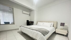Un dormitorio con cama, mesita de noche, lámpara, escritorio y ventana con persianas.