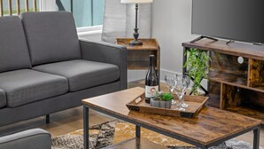 A modern living room with a grey sofa, a wooden coffee table with a bottle and glasses, and a TV on a wooden stand. - NEW Four Bedroom Nashville Downtown house to enjoy 2 mins to Broadway. (Nashville)
