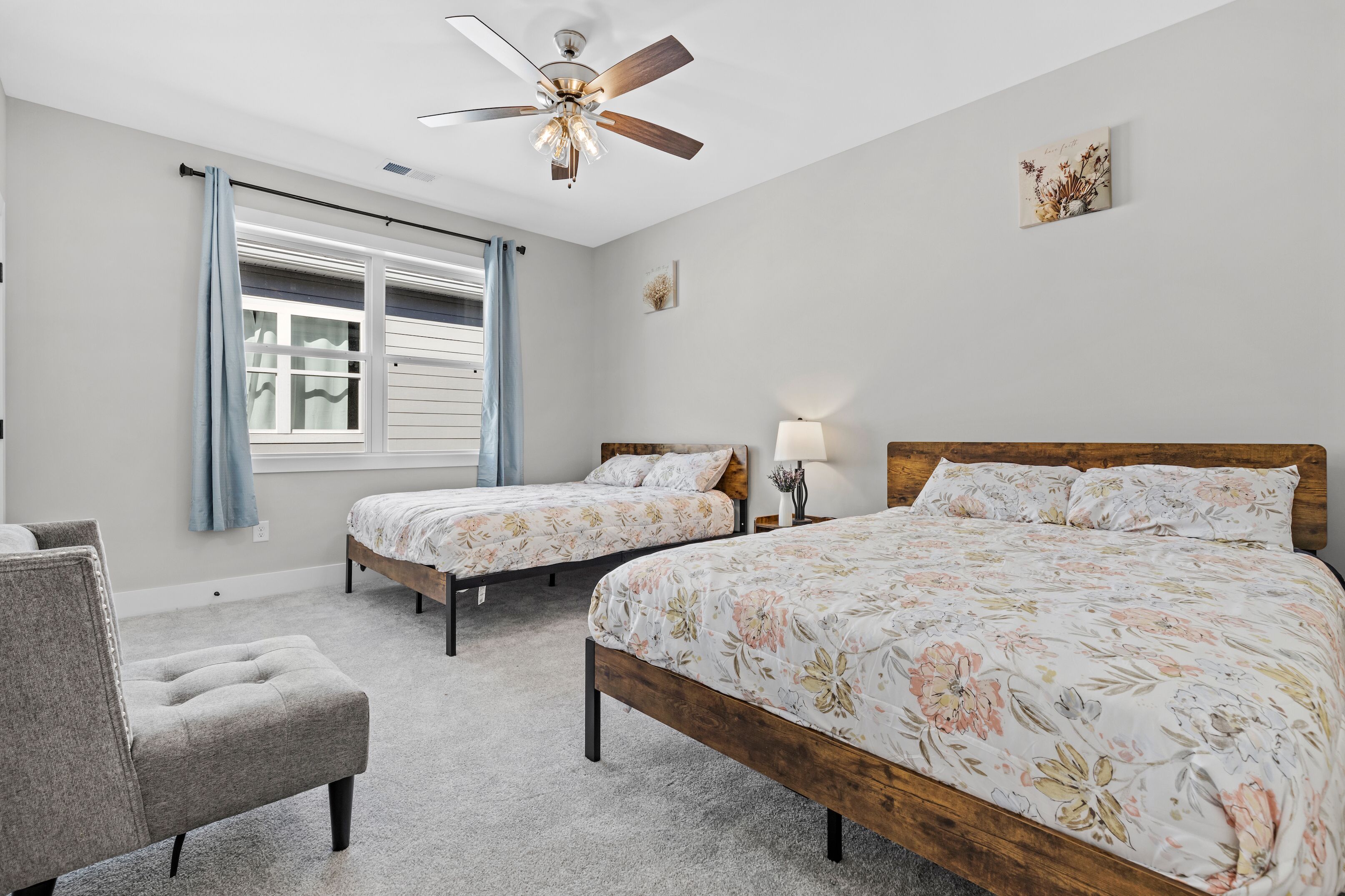 A bedroom with two single beds, a wooden headboard, a ceiling fan, a window with curtains, and a small bedside table with a lamp.