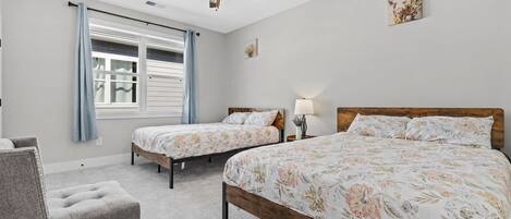 A bedroom with two single beds, a wooden headboard, a ceiling fan, a window with curtains, and a small bedside table with a lamp.