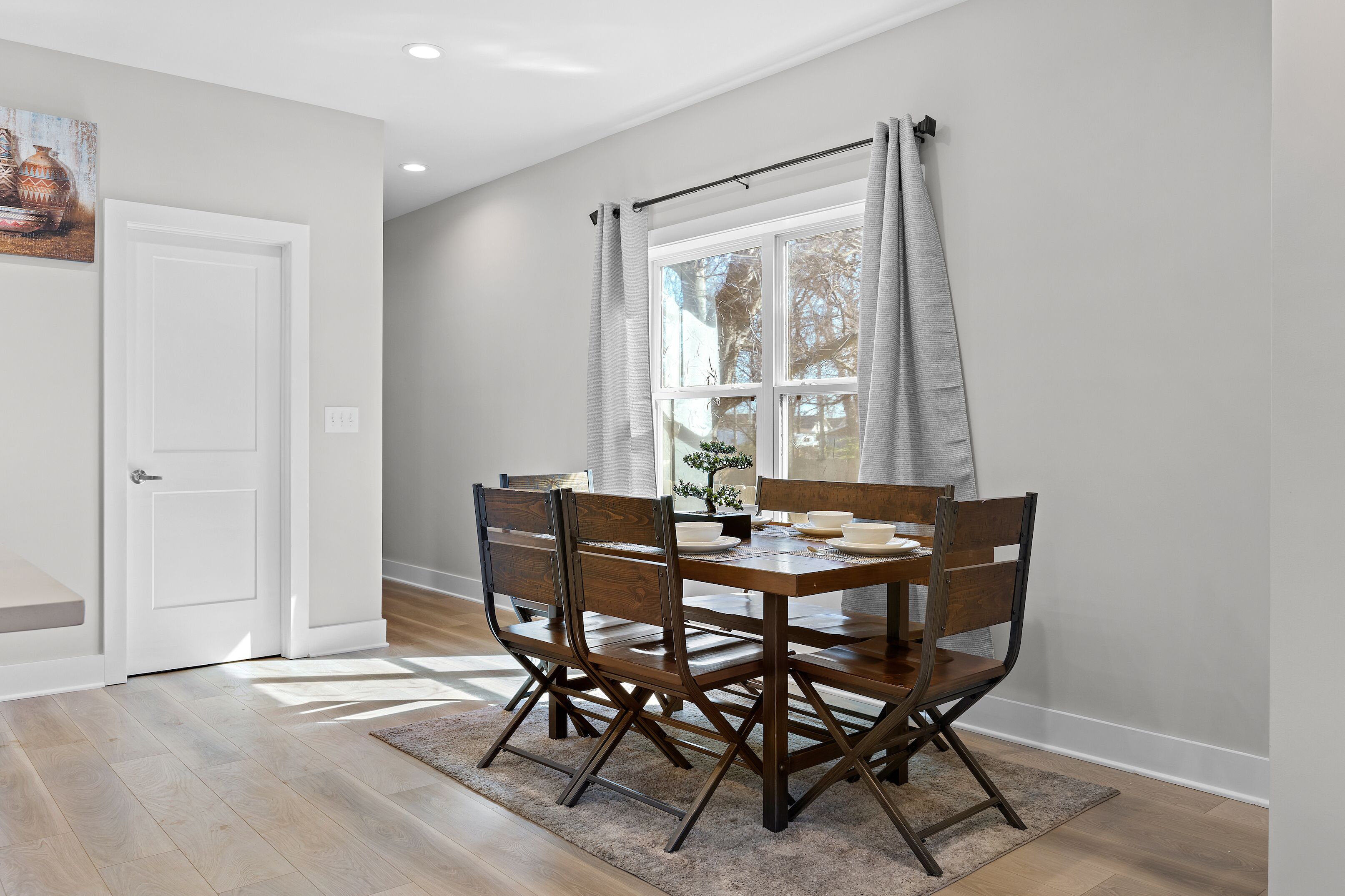 Un comedor con una mesa y sillas de madera, una ventana con cortinas y una puerta.