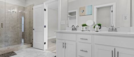 Un baño moderno con ducha a ras de suelo, un mueble de tocador amplio con espejo y una puerta que da a otra habitación.