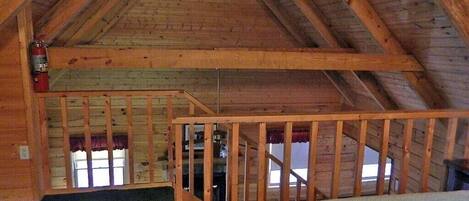 A wooden attic room with a sloped ceiling, a wooden staircase, and a fire extinguisher mounted on the wall.