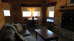 A cozy log cabin interior with a sofa set, a coffee table, a fireplace, and a television.