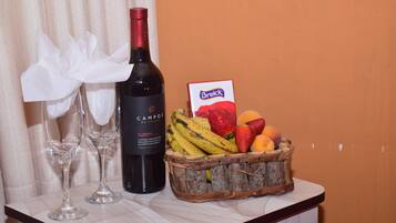 Una botella de vino, dos copas de vino vacías y una cesta de fruta sobre una mesa.