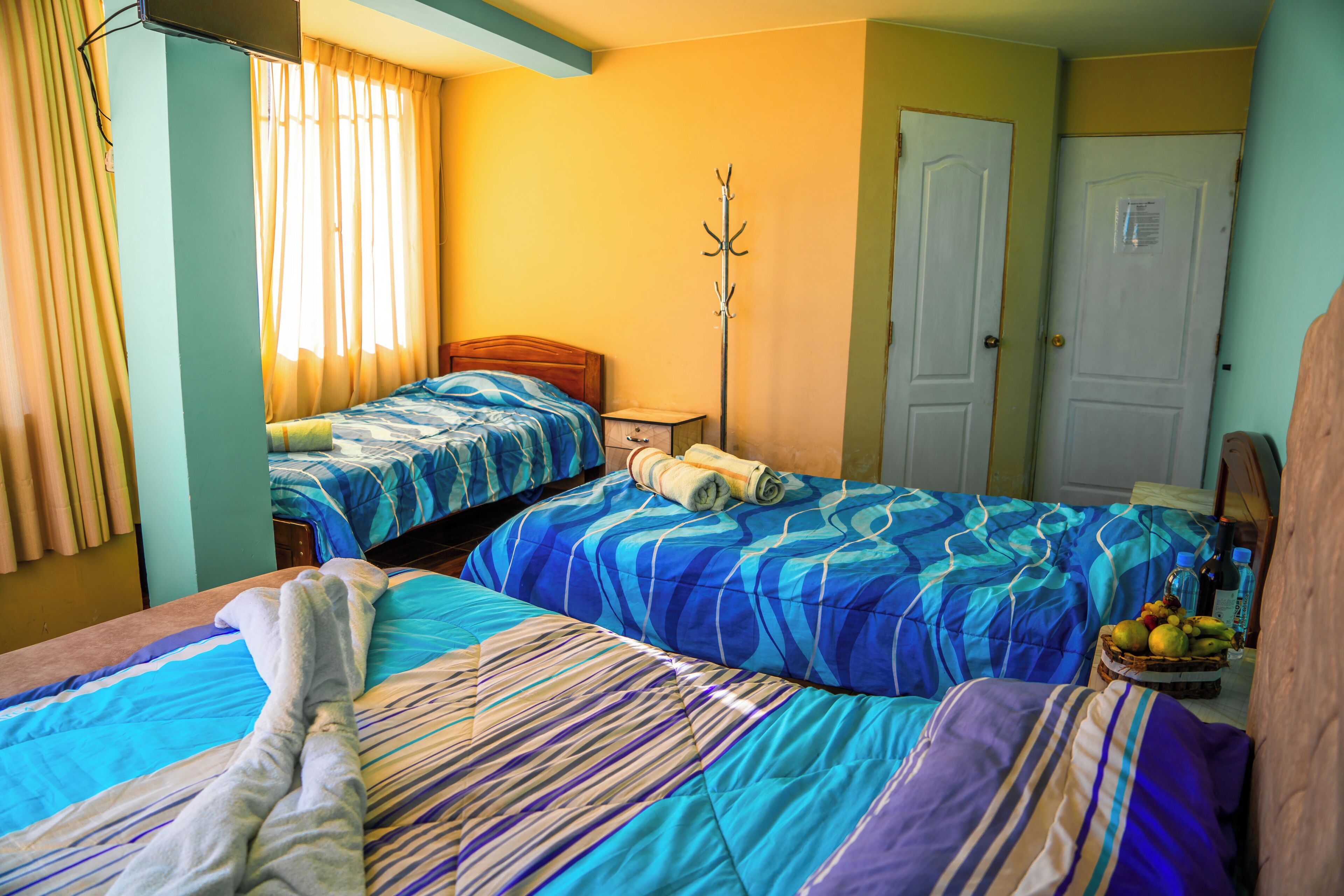 A hotel room with two beds, a wooden headboard, a bedside table, a lamp, and a fruit basket.