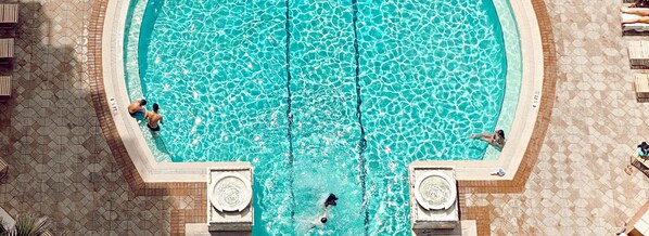 Vista aérea de una piscina rectangular con agua azul cristalina, rodeada por una solana con azulejos.