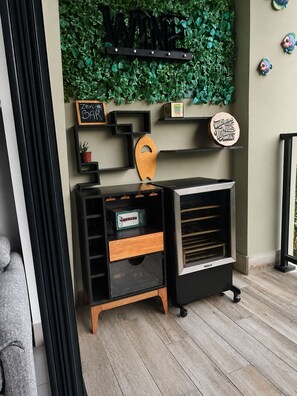 Une pièce avec un panneau mural indiquant « VIN », un meuble en bois avec des tiroirs, une petite étagère ornée d’objets décoratifs et un barbecue encastré.