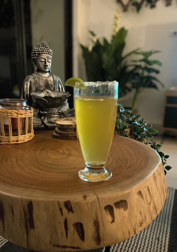A glass of yellow beverage on a wooden table with a Buddha statue and a small plant in the background.