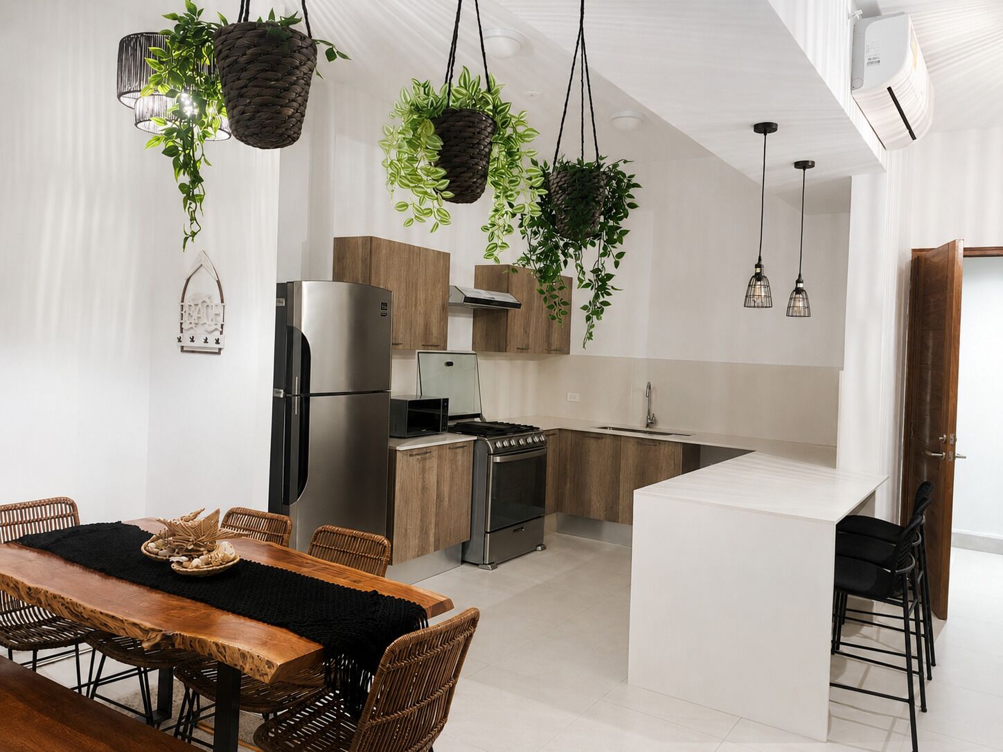 A modern kitchen with a central island, stainless steel appliances, and hanging plants.
