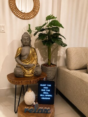 A Buddha statue on a wooden stool, a potted plant, a sofa, and a relaxation sign.