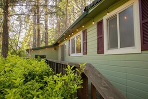 A green building with red shutters, surrounded by lush greenery and trees.