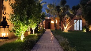 A pathway leading to a building with a door, surrounded by greenery and illuminated by lights. - Le Palais Averroes - Adults Only (Marrakech)