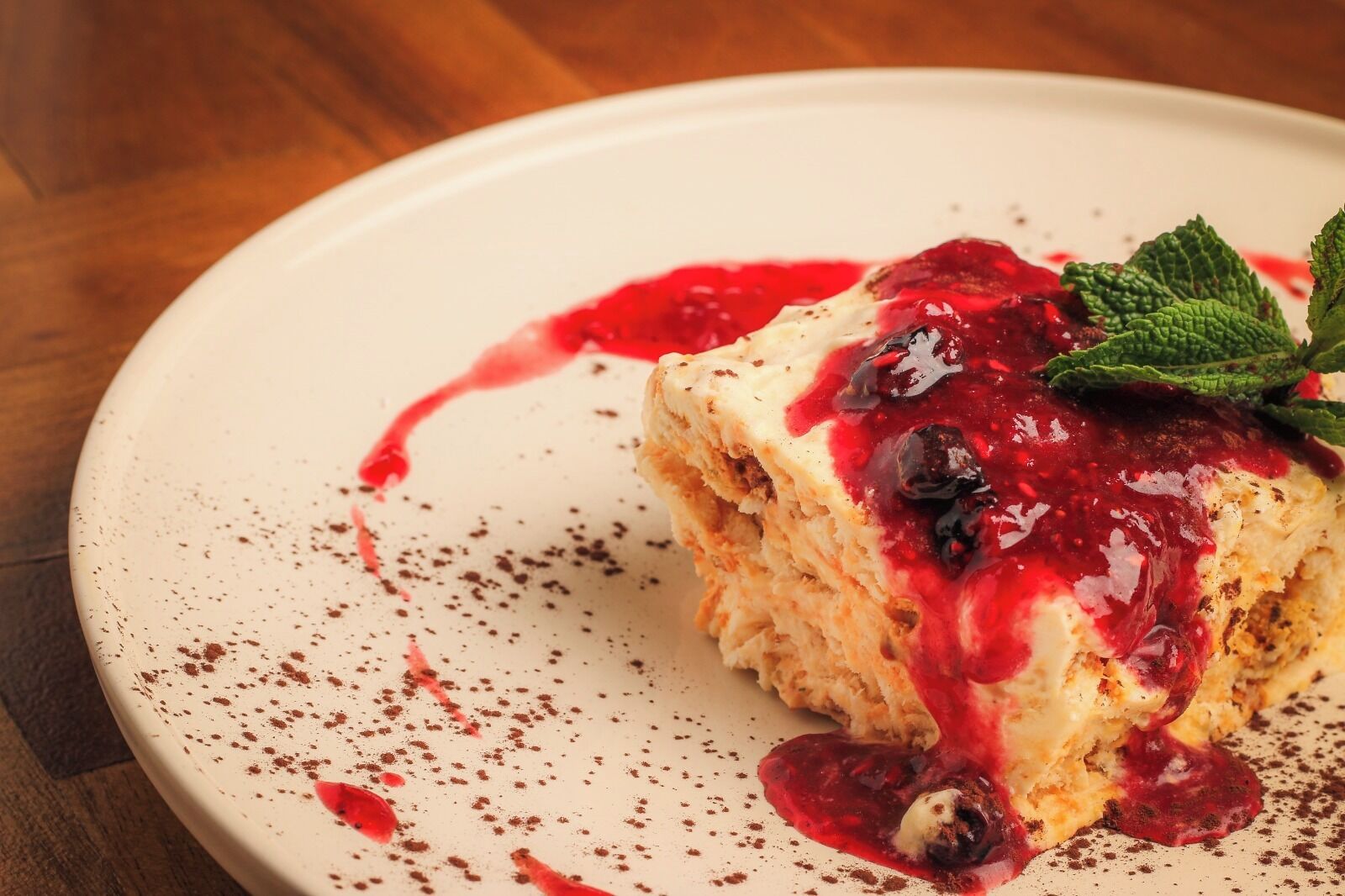 Un postre en un plato con compota de frutos rojos y adorno de menta.