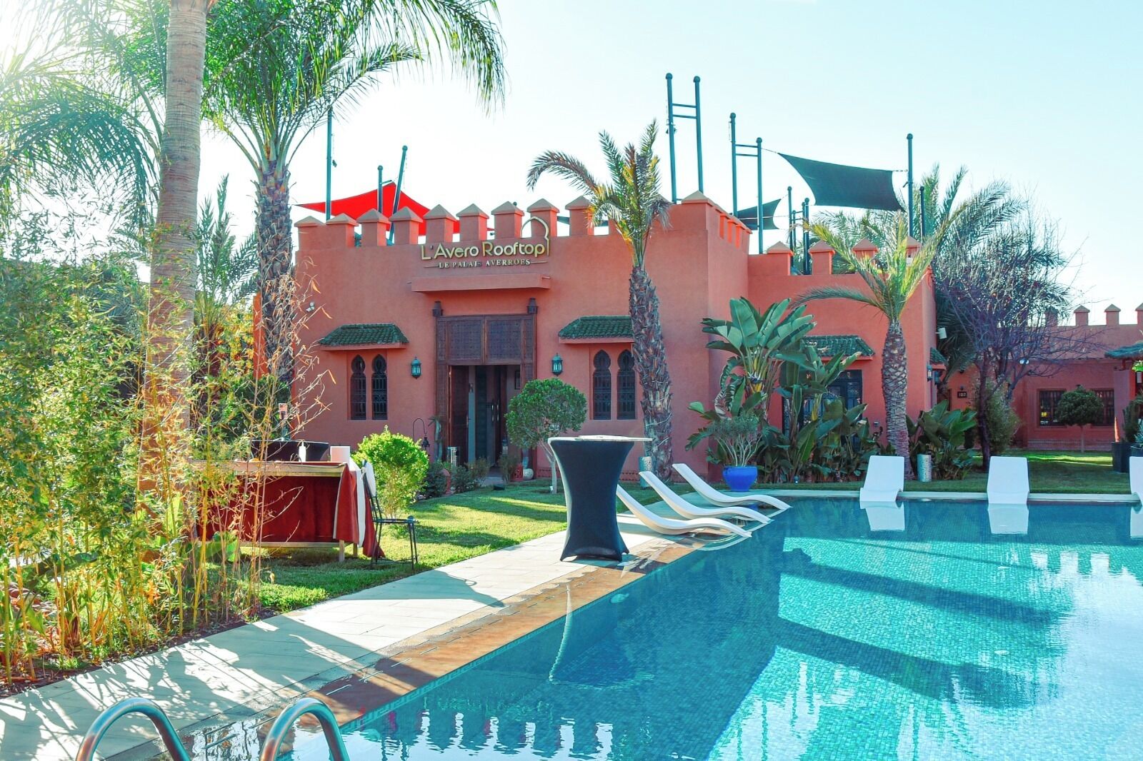 Un complexe hôtelier doté d’une piscine, de palmiers et d’un bâtiment à la façade rouge.