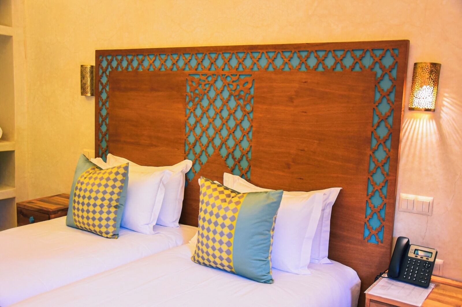 A hotel room with a large bed, two pillows, a bedside table with a phone, and a wall-mounted light fixture.