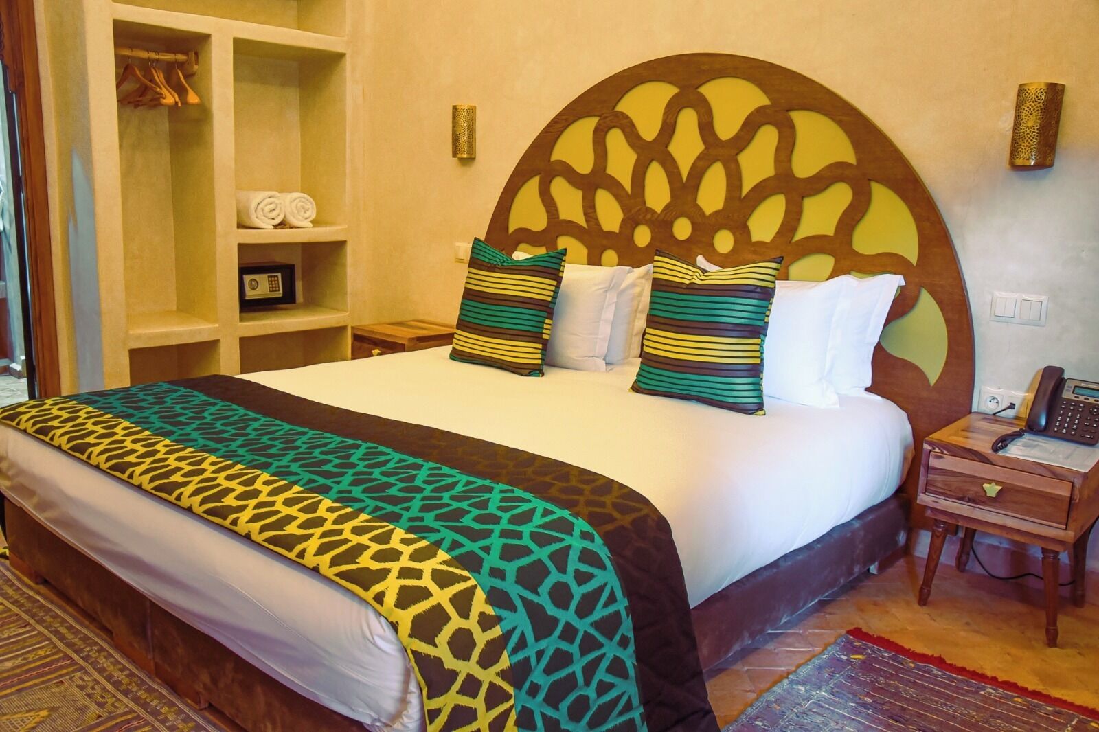 A hotel room with a large bed, a wooden headboard, a bedside table with a phone, and a wardrobe with hangers.