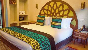 A hotel room with a large bed, a wooden headboard, a bedside table with a phone, and a wardrobe with hangers.