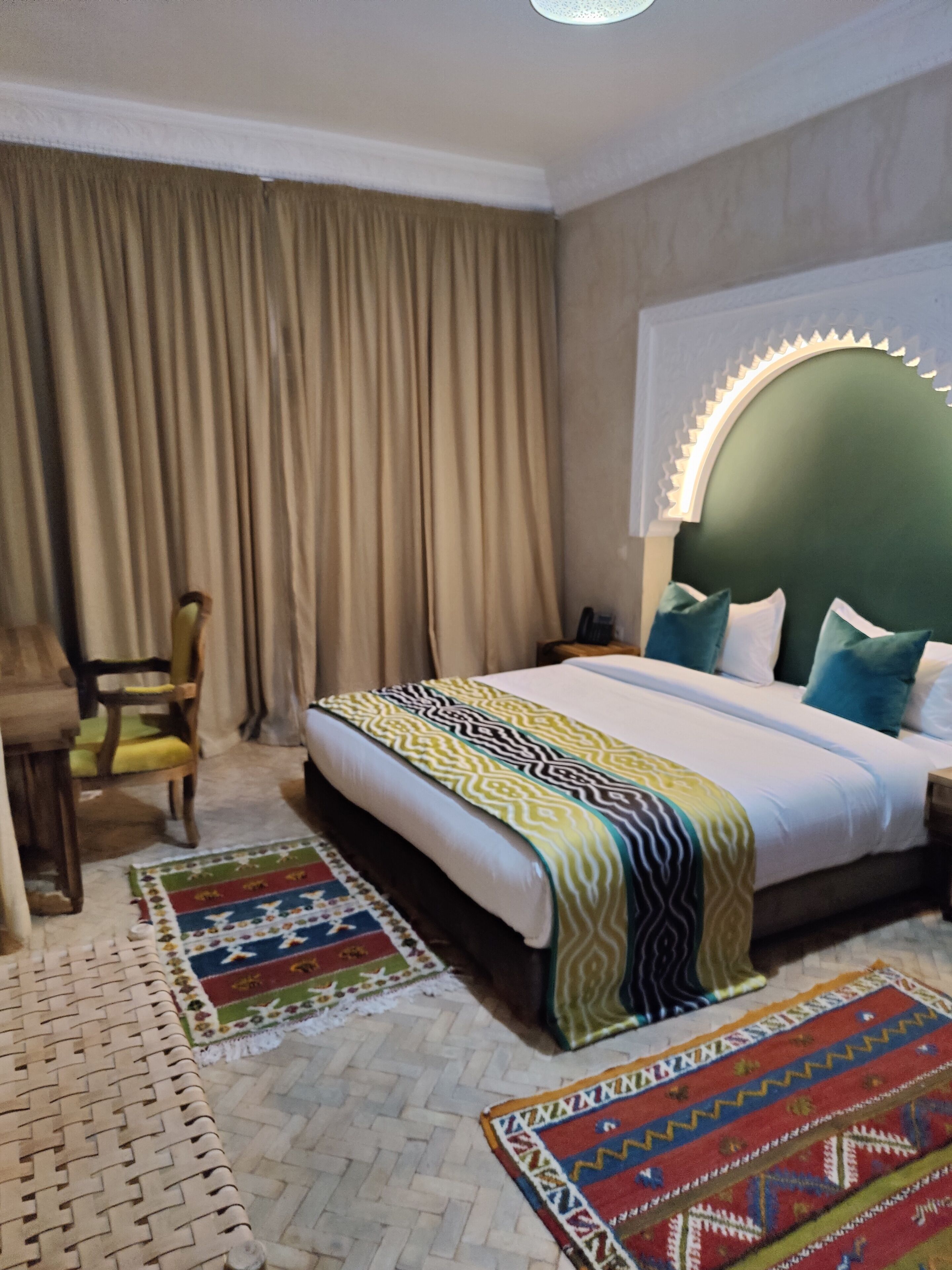 Una habitación de hotel con cama, una silla, una mesita de noche y una ventana con cortinas.