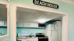 Una cocina con un letrero que dice 'BEACH HOUSE', armarios de madera, un microondas, una estufa y un refrigerador.
