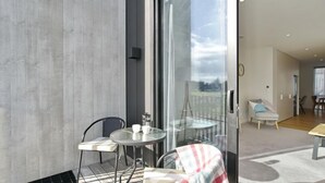 A modern living room with a glass door leading to a balcony. There is a round table with two chairs, a coffee maker, and a small plant on the balcony. - Worcester Terrace One -Top inner city location (Christchurch)