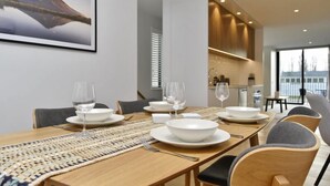 A modern dining area with a long wooden table set for four, white plates, bowls, and wine glasses. - Worcester Terrace One -Top inner city location (Christchurch)