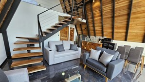 Una sala de estar moderna con una escalera, sofás grises y una zona de cocina.