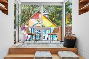 A modern outdoor seating area with a table and chairs, a potted plant, and a colorful mural in the background. - The Chavez Social Club | The Modern Backyard Pod (Austin)