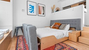 Un dormitorio moderno con cama, una silla, un escritorio y una estantería con objetos decorativos.