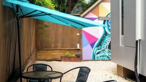 Un patio con mesa y sillas, un toldo azul y un mural colorido en la pared.