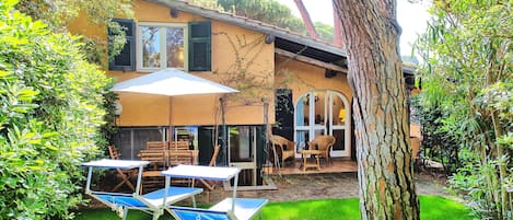 Una casa con un patio que tiene una mesa, sillas, un paraguas grande y un árbol.