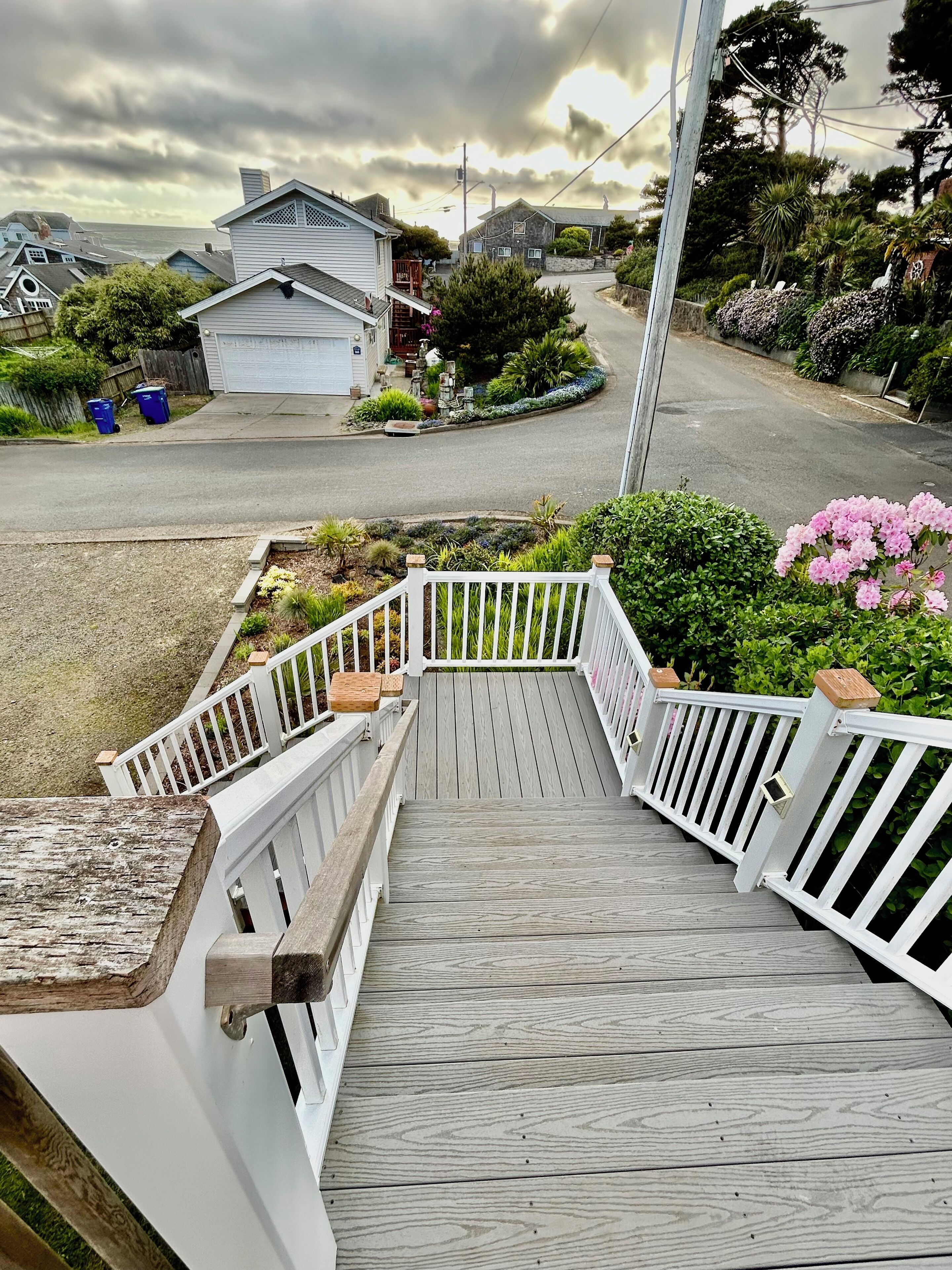 A wooden deck with white railings leading to a house with a garage.